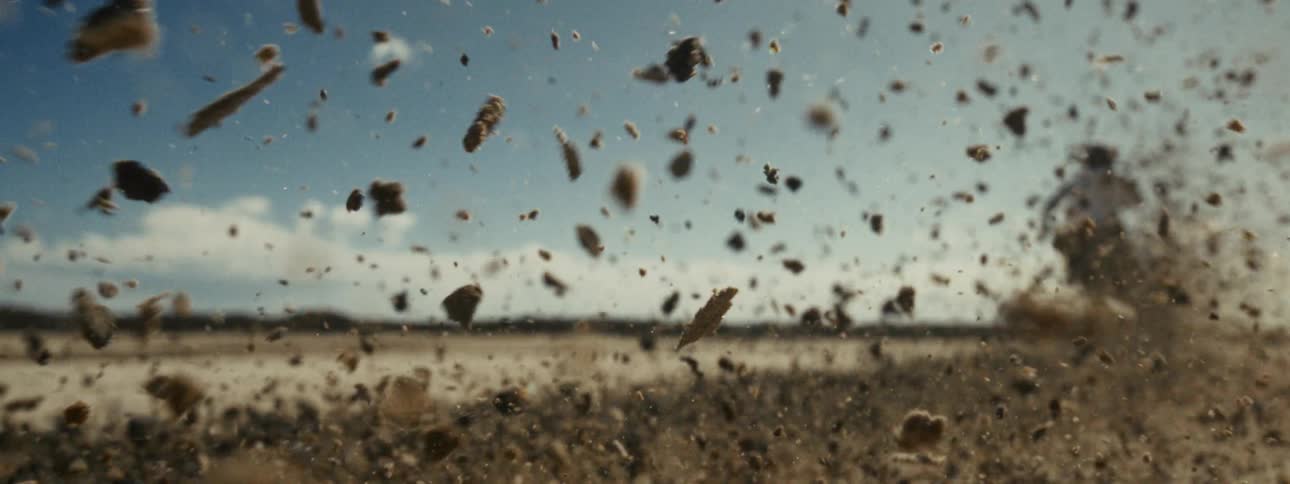 Dirt and rocks explode upwards in slow motion against a blurred desert landscape and blue sky