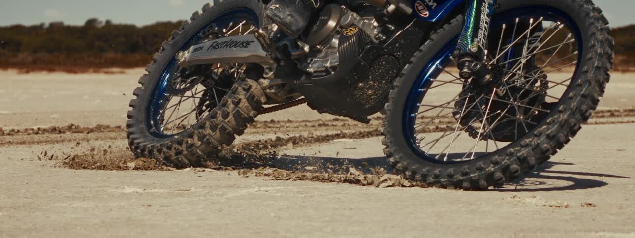 A super slow-motion close-up of a motocross bike's wheels spinning and kicking up sand on a dirt track