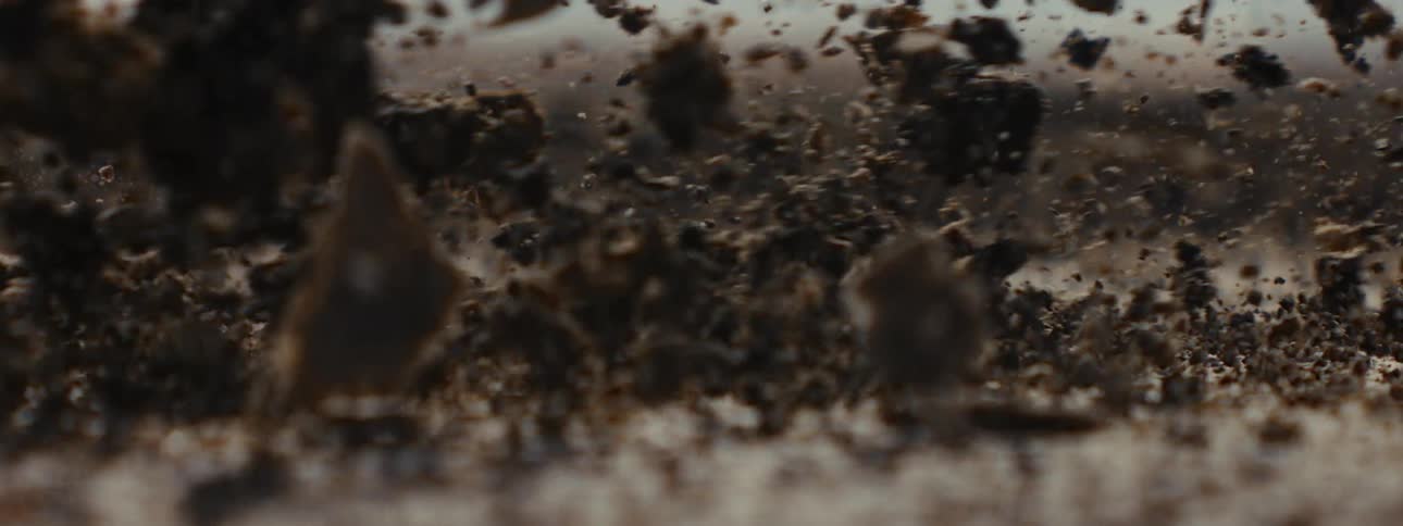 An extreme close-up slow-motion shot of a heavy treaded boot stomping on dry ground, sending dirt and debris flying into the air