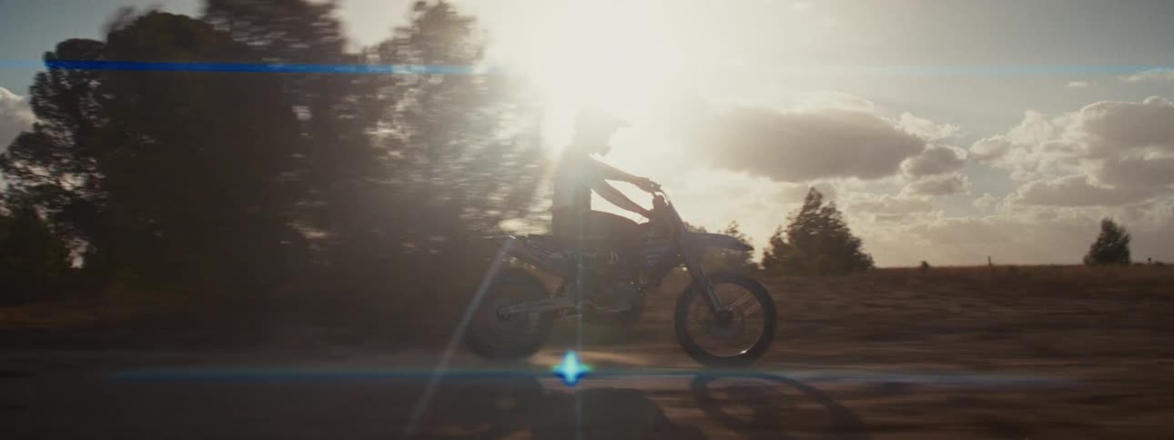 Cinematic slow motion shot of a motocross rider performing stunts and wheelies on a dirt track against the setting sun