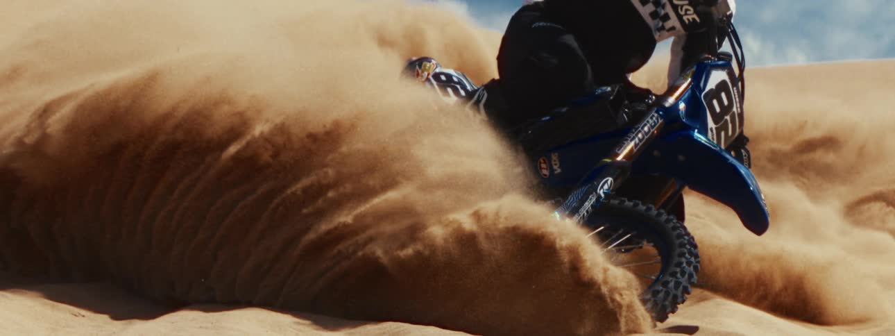 An extreme motocross rider kicks up a massive wave of sand while turning on a dune in super slow motion