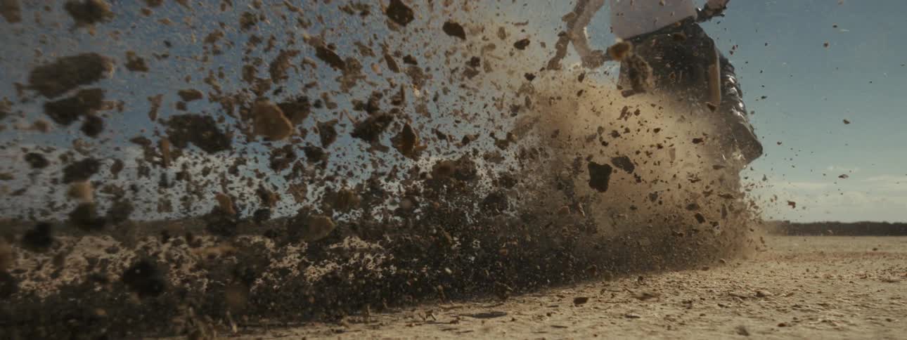 Dramatic slow-motion, low-angle shot of a motocross bike accelerating, kicking up a massive spray of dirt that flies towards the camera