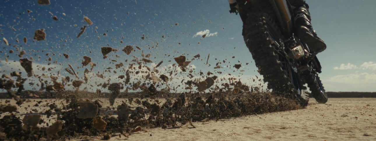 Close up slow motion shot of a motocross bike accelerating in the desert, kicking up dust and debris