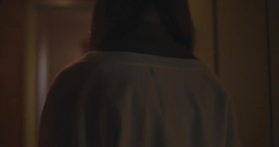 A young girl with a serious expression slowly opens the door and walks into her dimly lit home
