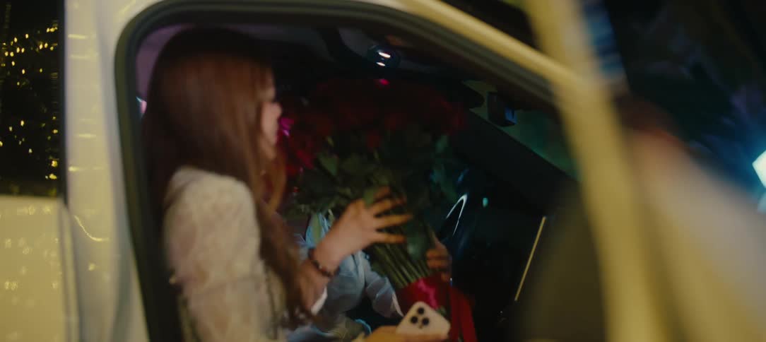 A handsome man surprises his girlfriend with a large bouquet of red roses as she gets into his car for a romantic date night
