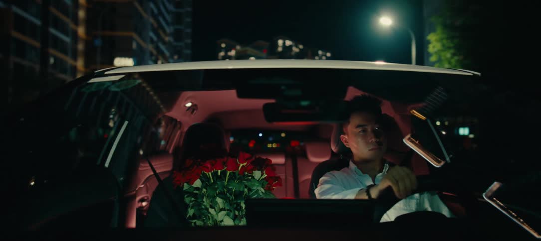 An Asian couple drives through the city at night with a large bouquet of red roses after a date