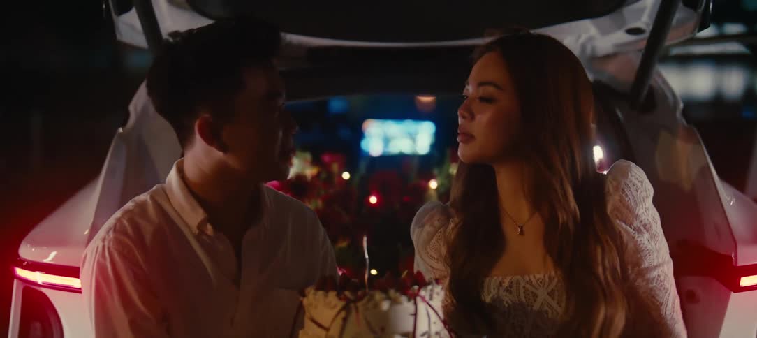 A sweet young couple kisses and playfully shares a birthday cake during a romantic celebration in the back of a car at night