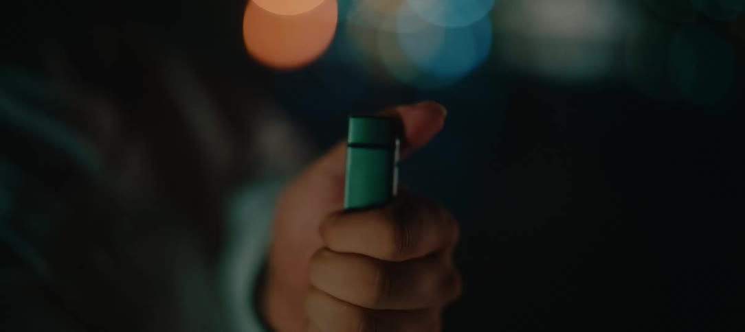 Slow motion close-up of a hand sparking a green lighter with a blue flame against a bokeh city lights background at night