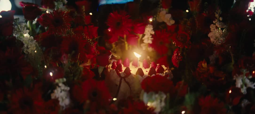 A romantic surprise at night featuring a car trunk filled with a beautiful bouquet of red flowers and a strawberry birthday cake with one lit candle