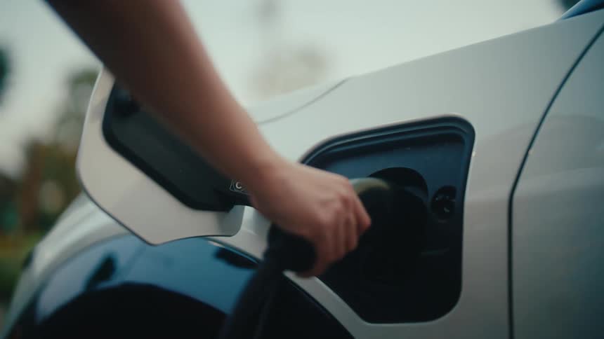 Slow motion close-up of a person plugging in an electric vehicle to charge