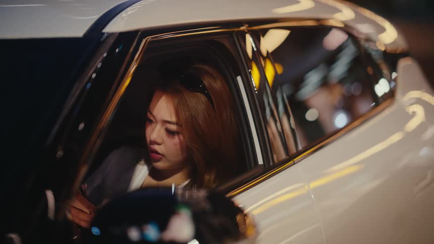A stylish young woman with sunglasses on her head fastens her seatbelt while sitting in a car at night