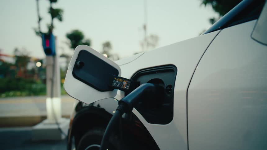 A close-up shot of a white electric vehicle plugged in and refueling its battery at a public EV charging station