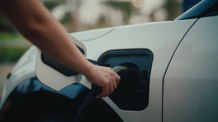 Slow-motion close-up of a woman's hand plugging a charger into the port of a white electric car
