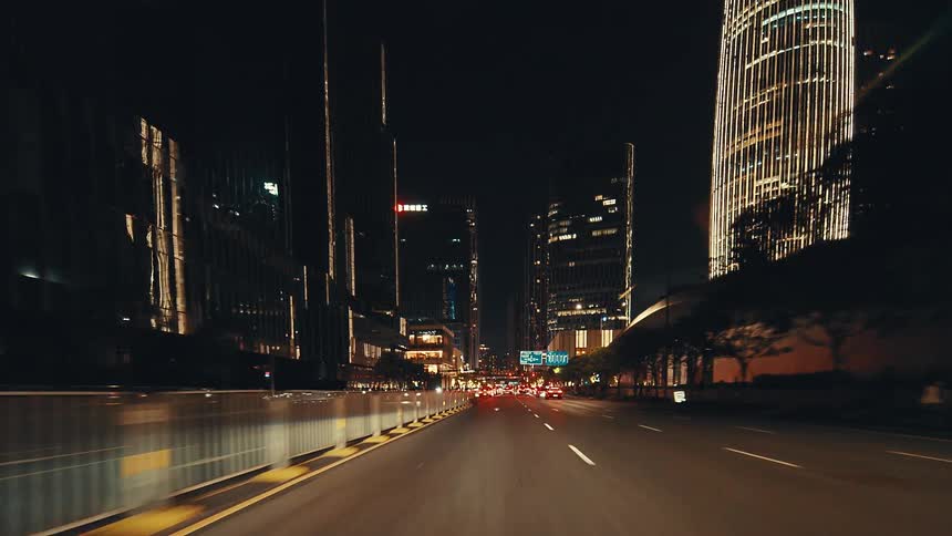 A point-of-view shot from a car driving through the glowing streets of a futuristic city at night surrounded by towering skyscrapers