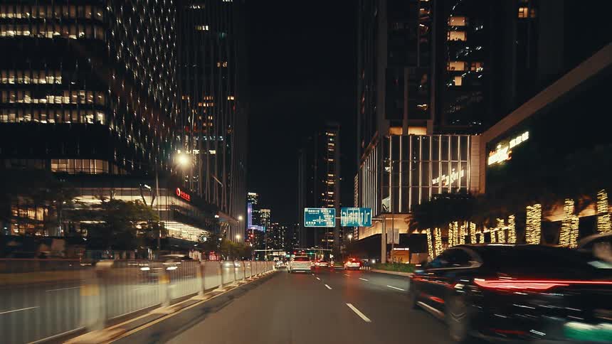 A smooth point-of-view drive through a vibrant, modern city at night surrounded by brightly lit skyscrapers