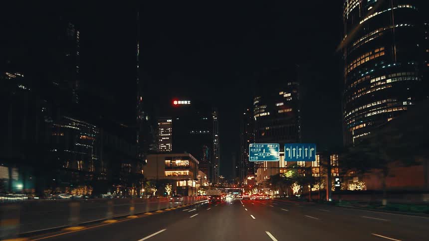 A POV shot driving through the illuminated streets of a modern metropolis at night, surrounded by towering skyscrapers and city traffic