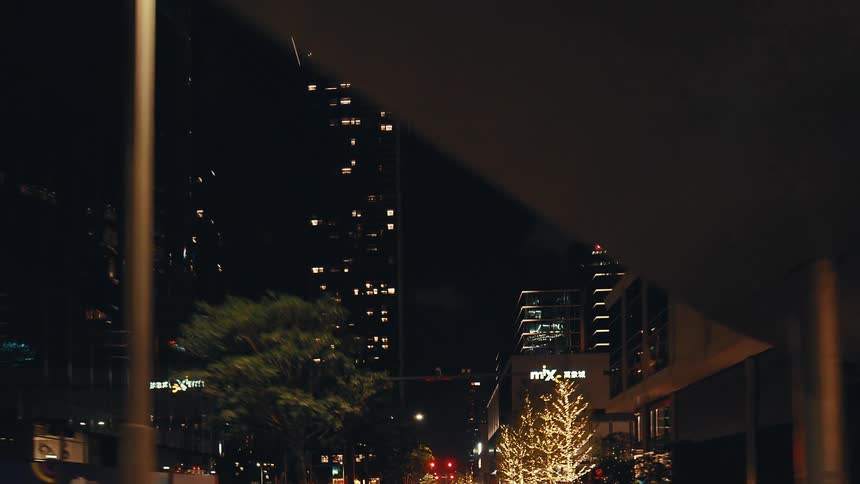 A slow-motion drive through a modern city at night, passing by skyscrapers and trees adorned with festive string lights