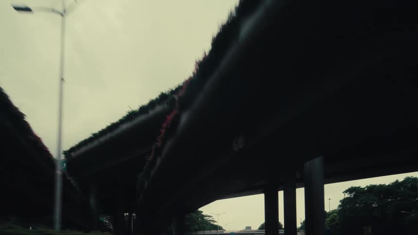 A moody, slow-motion drive under a complex series of concrete highway overpasses on an overcast day