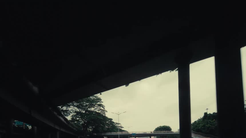 A moody, slow-motion drive under a complex series of concrete highway overpasses on an overcast day