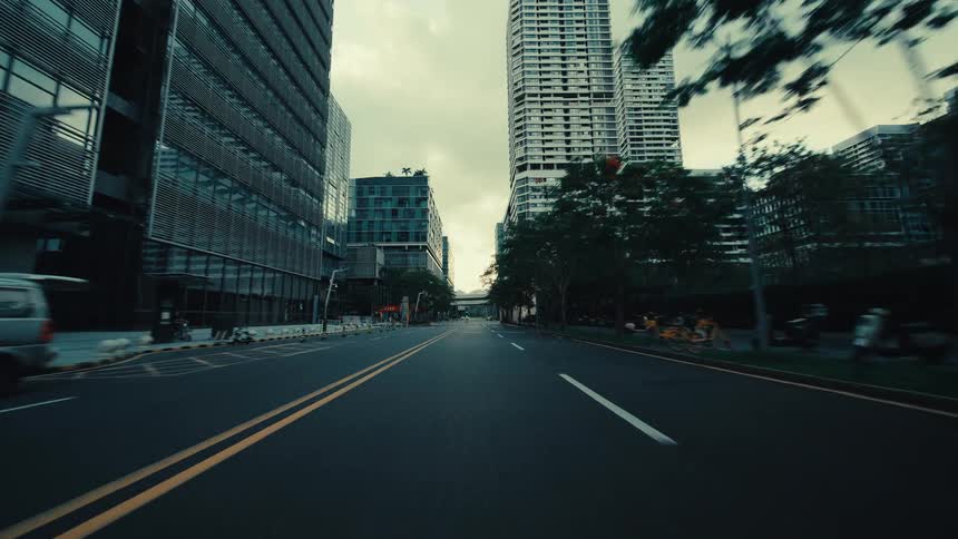 A smooth point-of-view drive down a modern city street, flanked by towering glass skyscrapers and contemporary apartment buildings on an overcast day