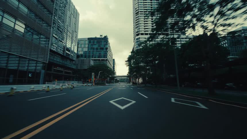 A smooth point-of-view drive down a modern city street, flanked by towering glass skyscrapers and contemporary apartment buildings on an overcast day