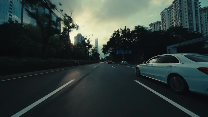 A first-person perspective of driving on a city highway in Guangzhou, China, passing under an overpass and through traffic under a dramatic sky