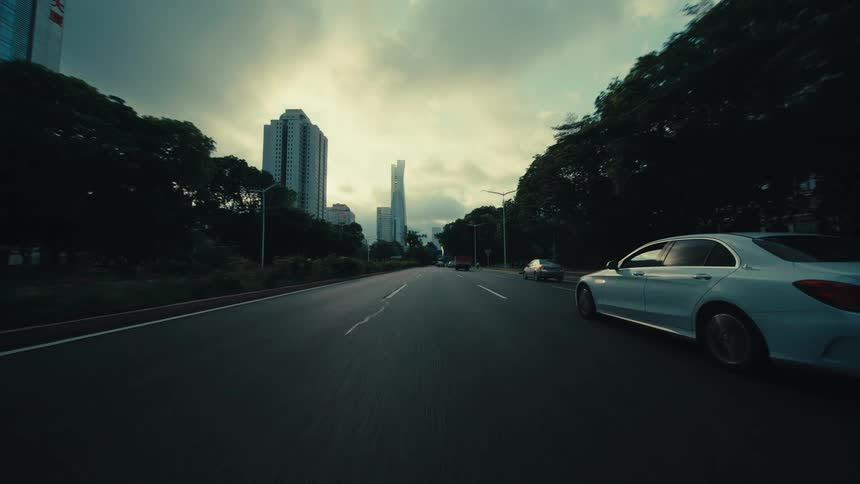A first-person perspective of driving on a city highway in Guangzhou, China, passing under an overpass and through traffic under a dramatic sky