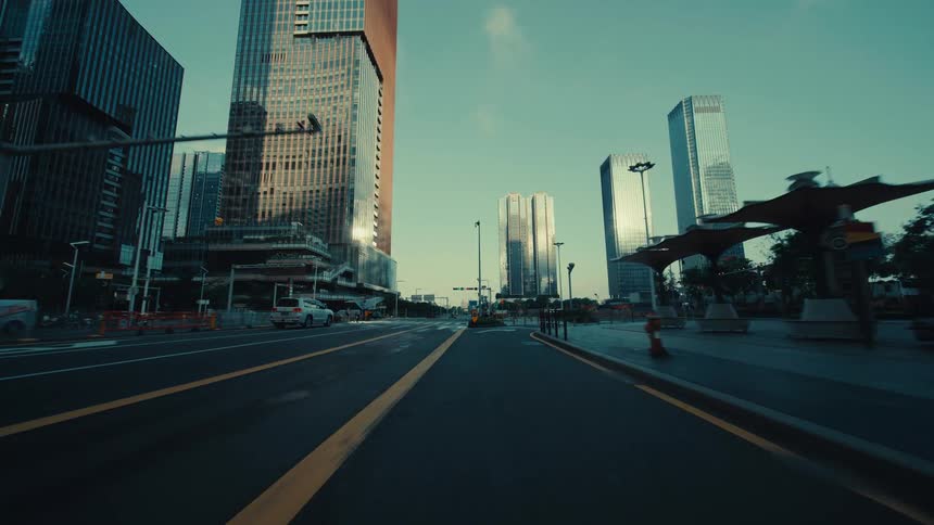 A slow, low-angle forward tracking shot travels down an empty city street surrounded by modern skyscrapers