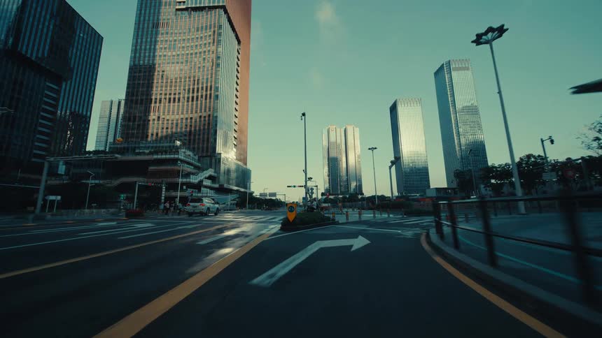 A slow, low-angle forward tracking shot travels down an empty city street surrounded by modern skyscrapers