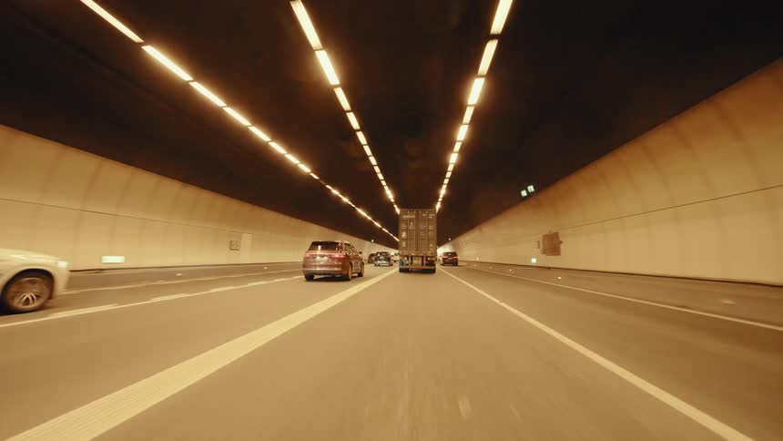 Point-of-view shot driving through a long, brightly lit highway tunnel following traffic