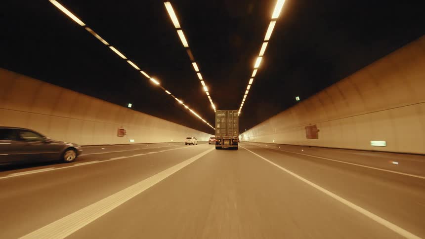 Point-of-view shot driving through a long, brightly lit highway tunnel following traffic