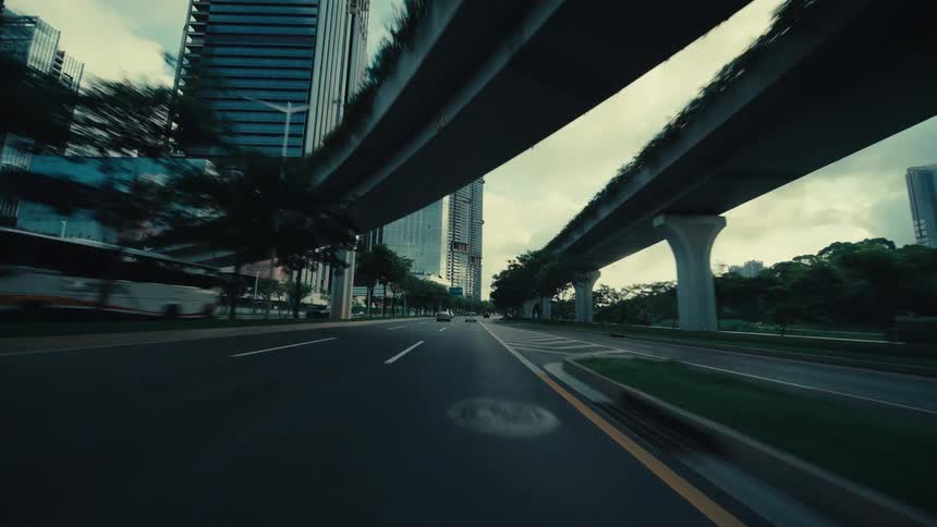 A dynamic point-of-view shot of driving out from under an overpass into a modern cityscape with skyscrapers