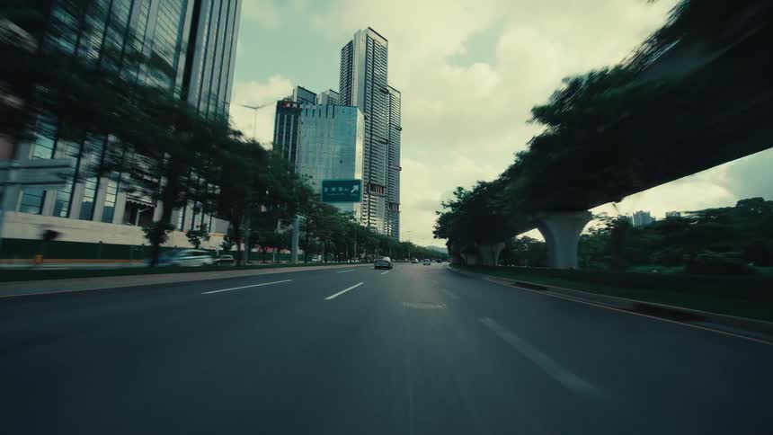 A dynamic point-of-view shot of driving out from under an overpass into a modern cityscape with skyscrapers