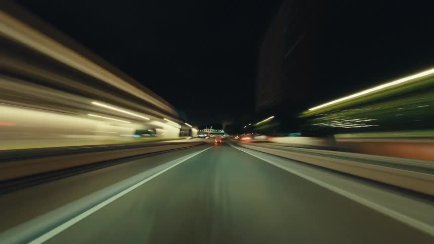 An exhilarating hyperlapse captures the blur of light trails from a car speeding through a city highway at night