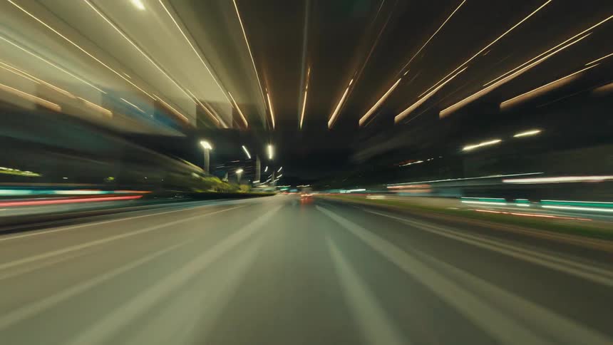 An exhilarating hyperlapse captures the blur of light trails from a car speeding through a city highway at night