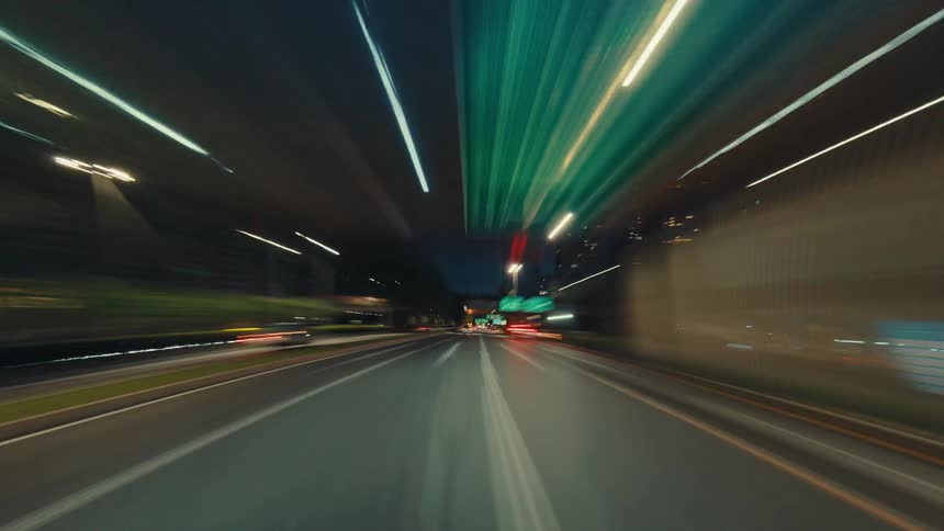 A dynamic point-of-view hyperlapse of driving through a modern city at night, with motion-blurred light trails creating a futuristic effect