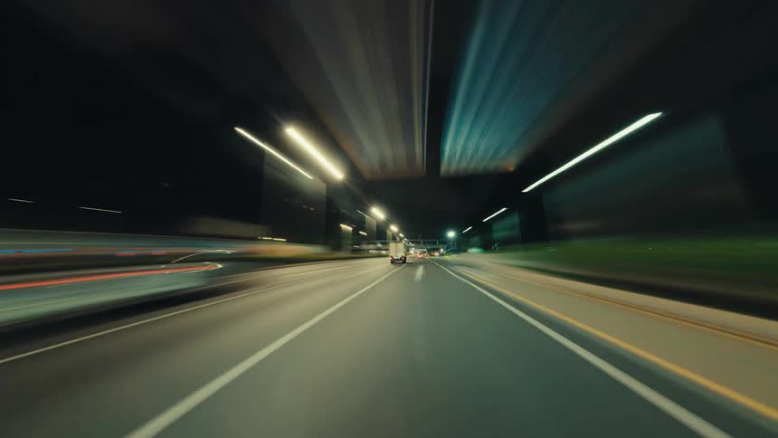 An exhilarating first-person hyper-lapse journey down a brightly lit city highway after dark, with motion blur creating streaks of light
