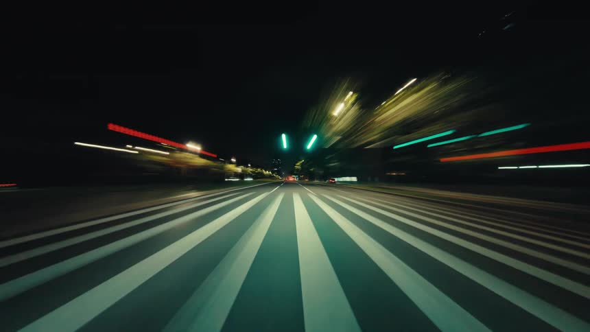 A dynamic point-of-view hyperlapse shows a high-speed drive through a city at night as lights streak by