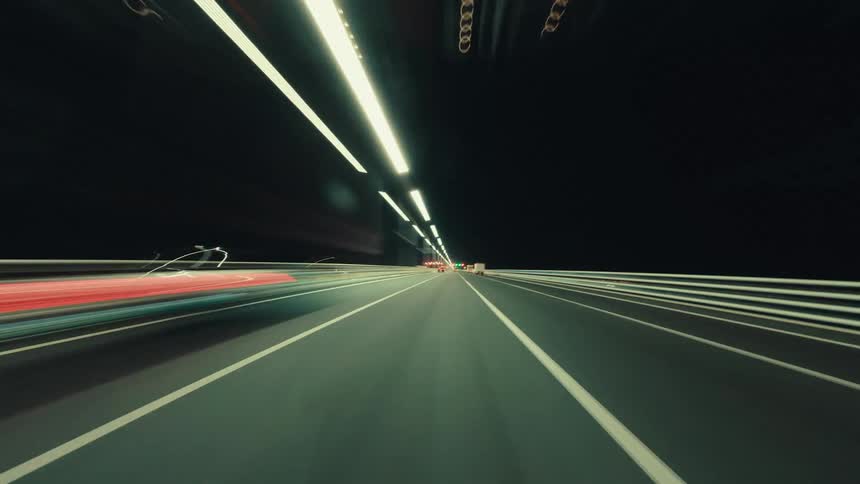 A futuristic time-lapse POV of driving at high speed through an illuminated highway tunnel at night