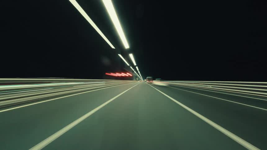 A futuristic time-lapse POV of driving at high speed through an illuminated highway tunnel at night