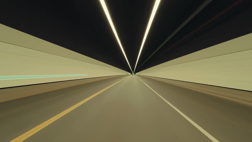 A futuristic point-of-view time-lapse captures a high-speed drive through brightly lit highway tunnels at night