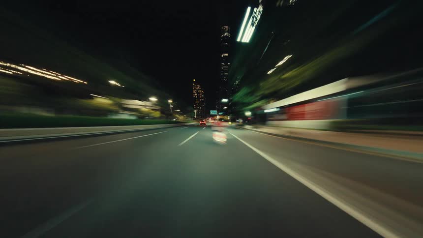 An exhilarating FPV hyperlapse captures the blur of city lights while driving at high speed down an empty road at night
