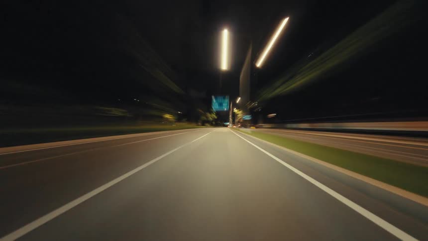 An energetic hyperlapse captures the blur of city lights from a car speeding down a highway late at night