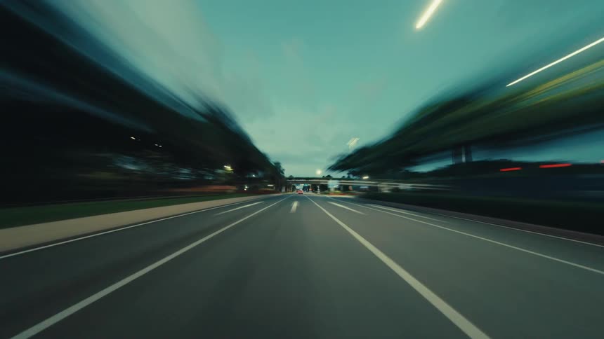 A futuristic point-of-view hyperlapse shows a car speeding down a city highway at night as lights blur into streaks