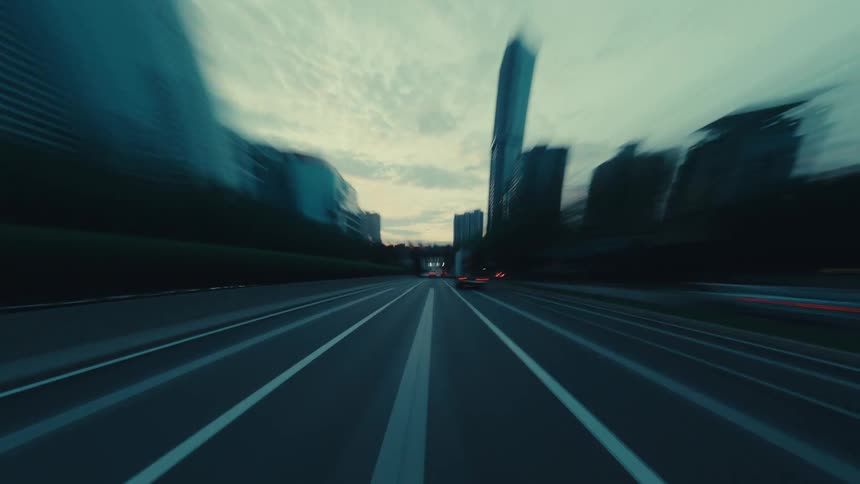 A fast-paced point-of-view hyper-lapse driving through a modern city highway at dusk with streaking light trails and motion blur