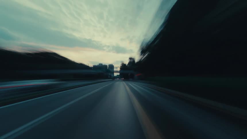 A fast-paced point-of-view hyper-lapse driving through a modern city highway at dusk with streaking light trails and motion blur