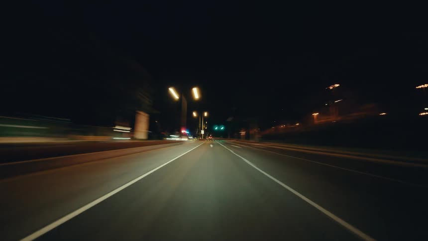 A fast-paced point-of-view hyperlapse shows a car speeding down city streets at night, creating mesmerizing light trails