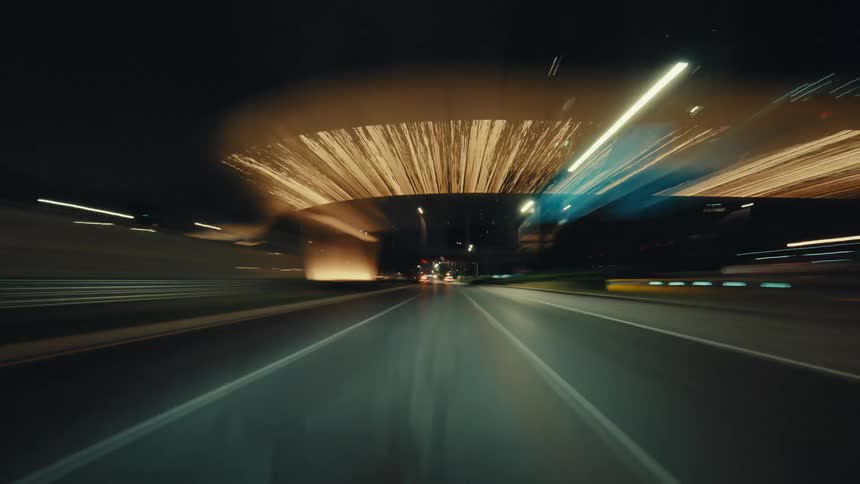 A thrilling first-person perspective hyperlapse captures a high-speed drive through a modern city at night, with streetlights blurring into streaks of light