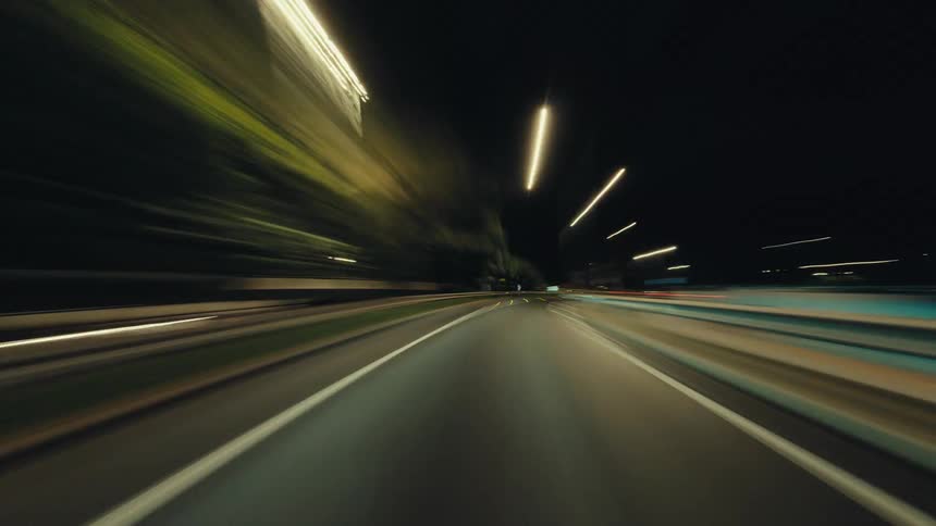 POV hyperlapse of a car speeding through a modern tunnel and along city highways at night, creating colorful light streaks