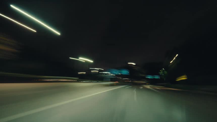 Fast-paced hyper-lapse shot from a car speeding down an empty highway at night with blurry light trails